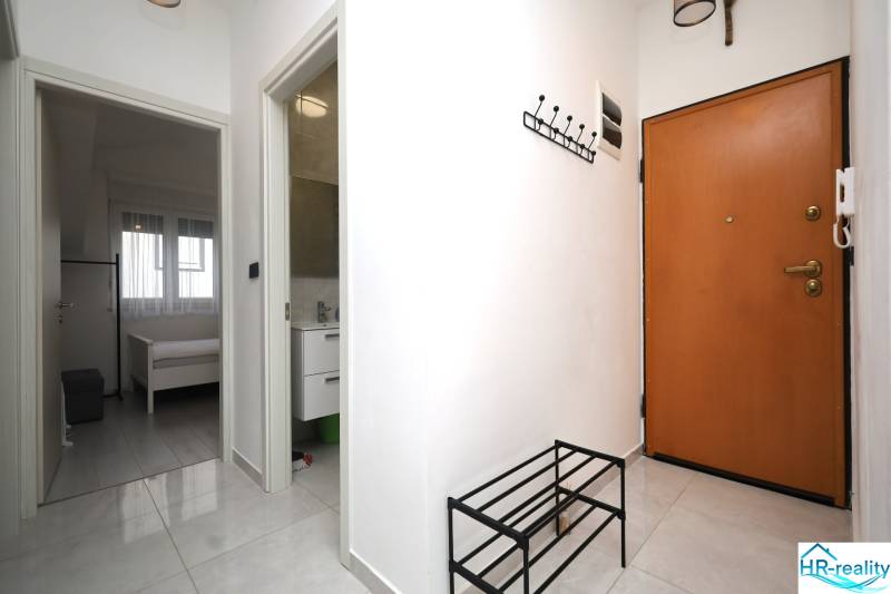 Rekreační apartmán s dlažbou, věšákem, otevřenými dveřmi do ložnice a koupelny.