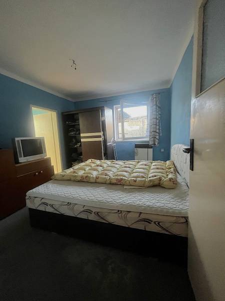 Ložnice s postelí, tmavou skříní, televizí a modrými stěnami v rodinném domě.