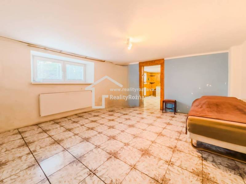 Pokoj s dlažbou v rodinném domě, postel u stěny, okno s radiátorem.