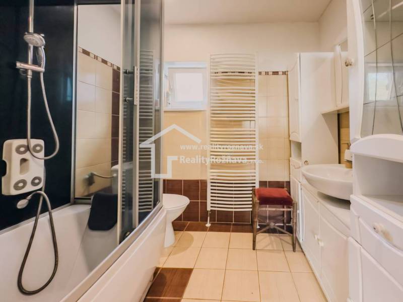 Koupelna v rodinném domě s vanou, sprchou, umyvadlem a radiátorem.