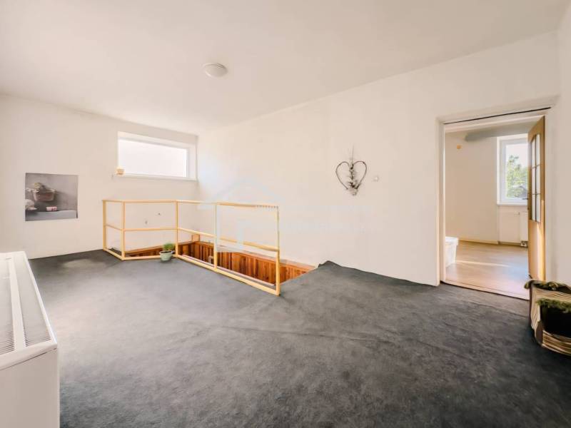 Interiér rodinného domu s kobercem, schodištěm a jednoduchou dekorací na stěně.