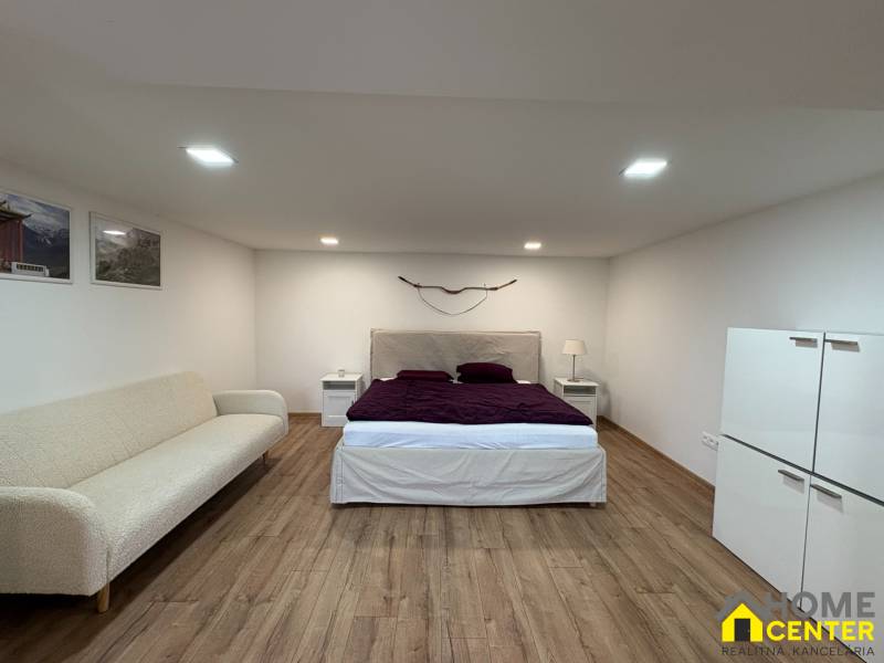 Interiér 1-pokojového bytu s postelí, pohovkou a podlahou s dřevěným dekorem.