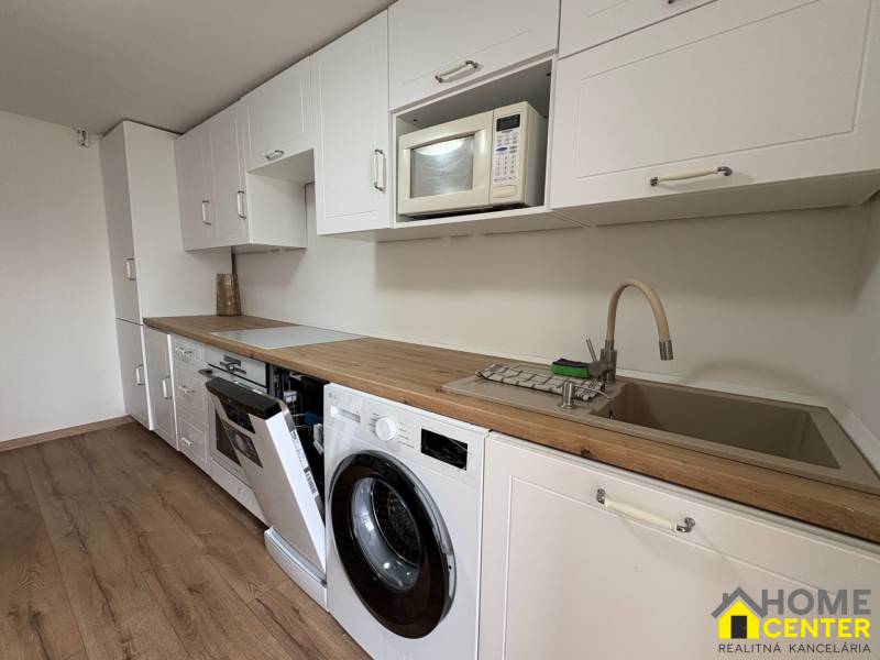 Kuchyně v 1-pokojovém bytě s bílou linkou, pračkou a podlahou s dřevěným dekorem.
