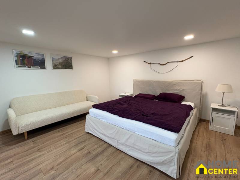 Ložnice v jednopokojovém bytě s pohovkou, postelí a podlahou s dřevěným dekorem.