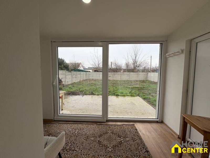 Pokoj jednopokojového bytu s výhledem na zahradu a podlahou s dřevěným dekorem.