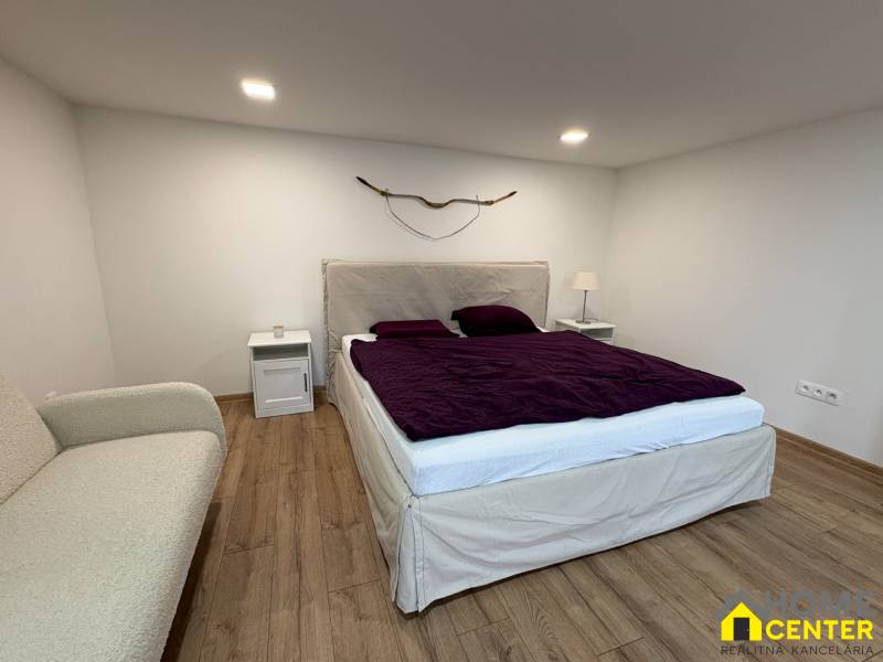 Ložnice v 1-pokojovém bytě s podlahou s dřevěným dekorem, postelí a dekorativním prvkem na stěně.