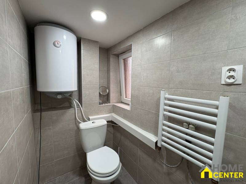 Koupelna v 1-pokojovém bytě se sanitou, bojlerem a bílým žebříkovým radiátorem.