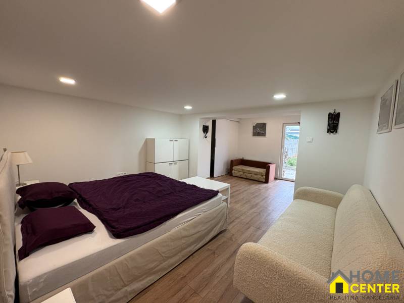 Ložnice v jednopokojovém bytě s podlahou s dřevěným dekorem, jednoduchý nábytek a dekorace.