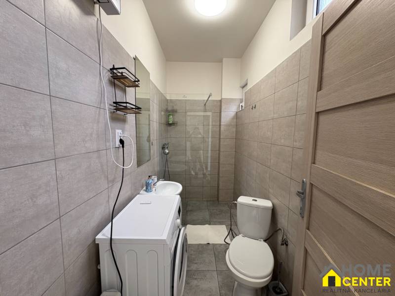 Koupelna v 1-pokojovém bytě s pračkou, umyvadlem a sprchovým koutem v neutrálních odstínech.