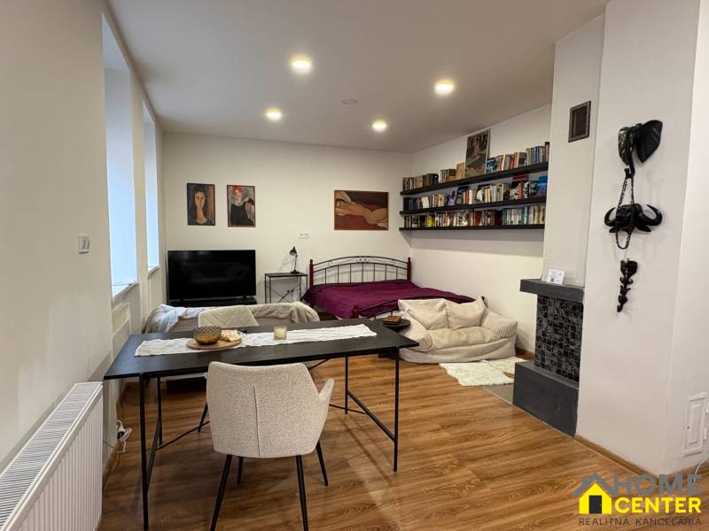 Interiér 1-pokojového bytu s podlahou s dřevěným dekorem, postelí a jídelním stolem.