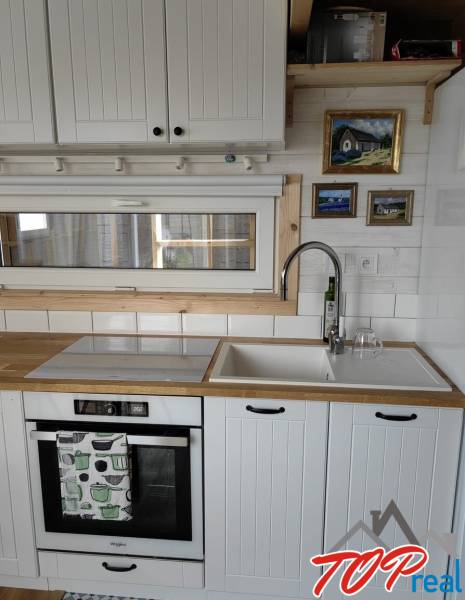 Kuchyňská linka v rodinném domě s bílými skříňkami, dřezem a vestavnou troubou.