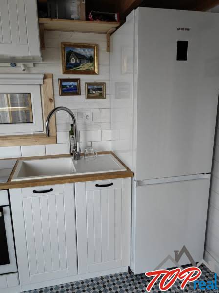 Kuchyně v rodinném domě s bílou linkou, lednicí a uměleckými obrazy na stěně.