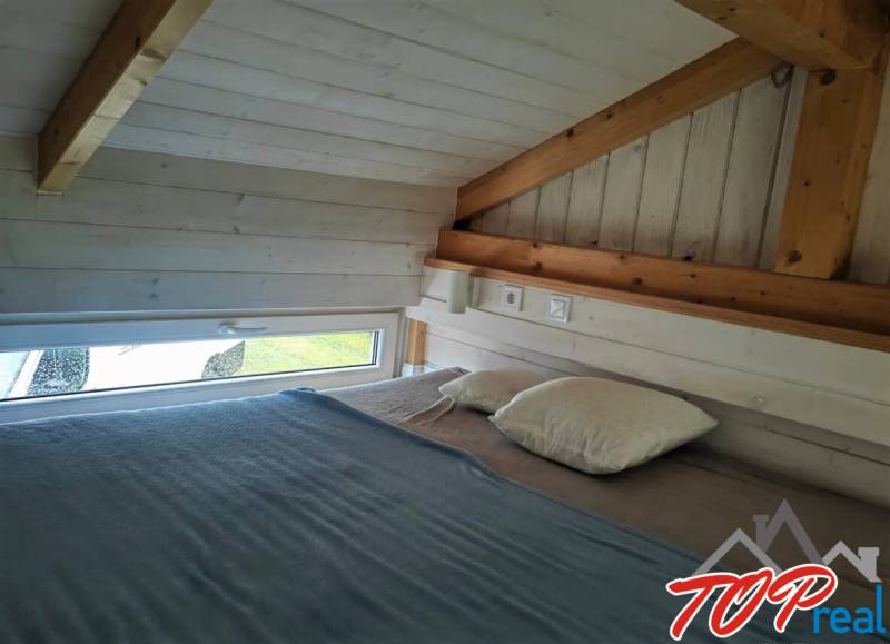 Podkrovní ložnice s dřevěnými trámy a malým oknem v rodinném domě.