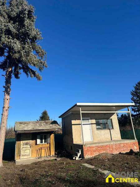 Zahrady v Nové osadě v Komárně s malými stavbami a jehličnatým stromem.