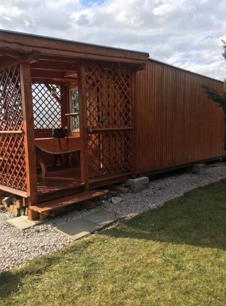 Dřevěná chata v Kráľovej nad Váhom s malou vyvýšenou terasou a trávníkem.