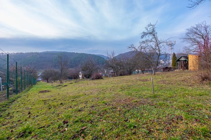 Zahrada s výhledem na kopce a chatu v Prešově, obklopená stromy a plotem.