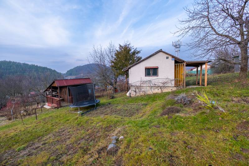 Chata v Prešově obklopená stromy, s výhledem na kopce a trampolínou v zahradě.