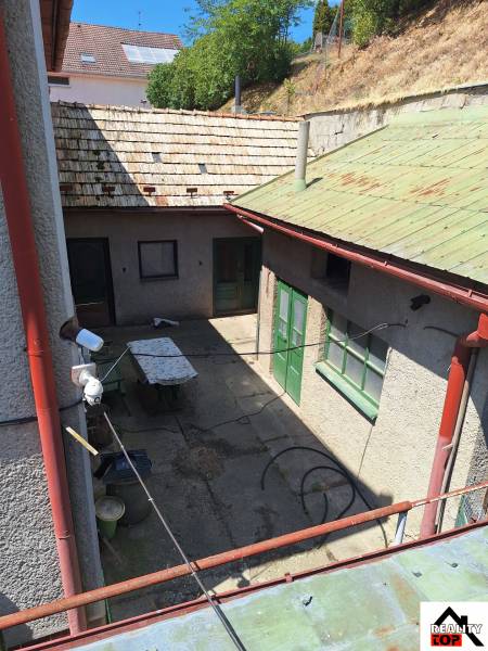 Dvůr rodinného domu v Tachtoch s viditelnými dveřmi, stolem a travnatým svahem.