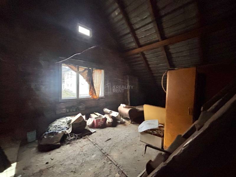 Podkrovní místnost s oknem v rodinném domě plná starých předmětů a nábytku.