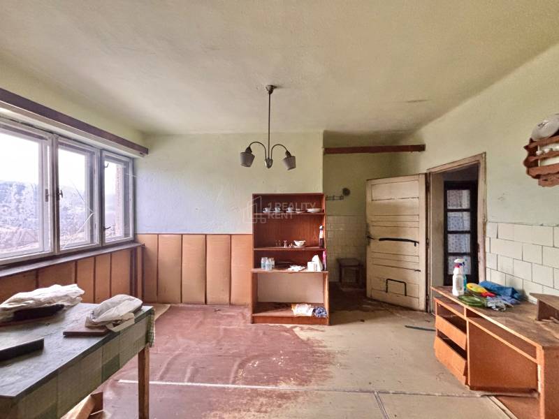 Pokoj v rodinném domě s nábytkem, poličkami a velkým oknem.