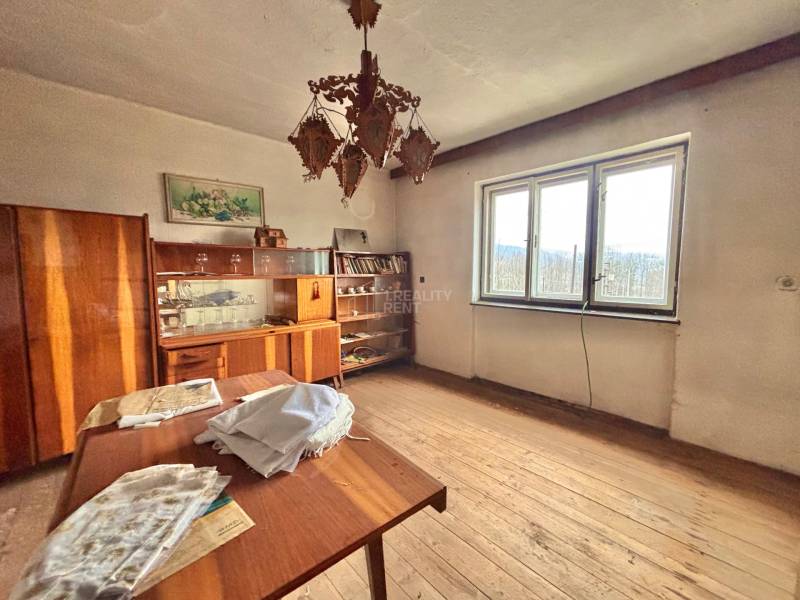 Pokoj v rodinném domě s dřevěným dekorem, vintage nábytkem, lustrem a velkým oknem.