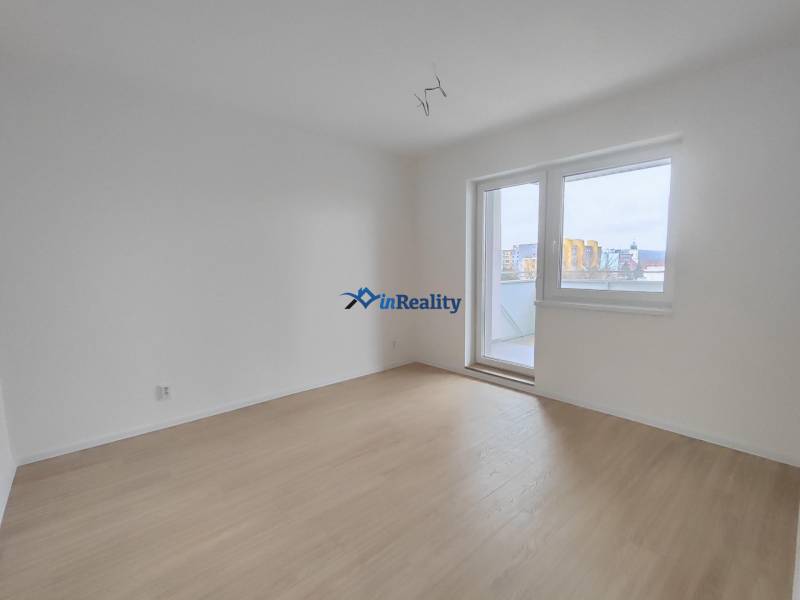 Prázdný pokoj v 2pokojovém bytě s podlahou s dřevěným dekorem a balkónovými dveřmi.