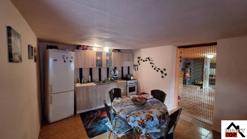 Kuchyně v rodinném domě s jídelním stolem, kuchyňskou linkou a lednicí.