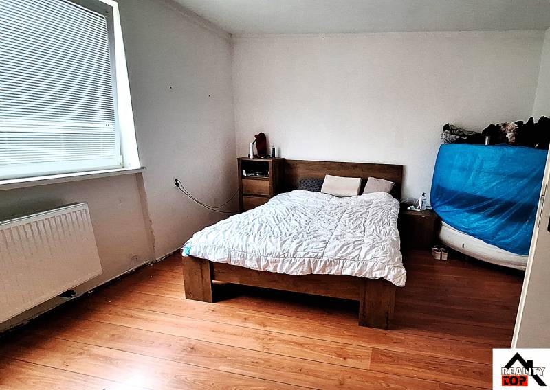 Ložnice v rodinném domě s postelí, komodou a podlahou s dřevěným dekorem.