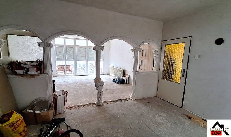 Interiér rodinného domu s klenutými oblouky a prosklenými dveřmi. Probíhají opravy.