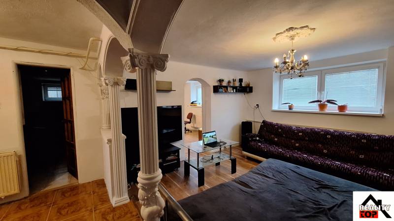 Obývací pokoj v rodinném domě s pohovkou, skleněným stolem a sloupy.