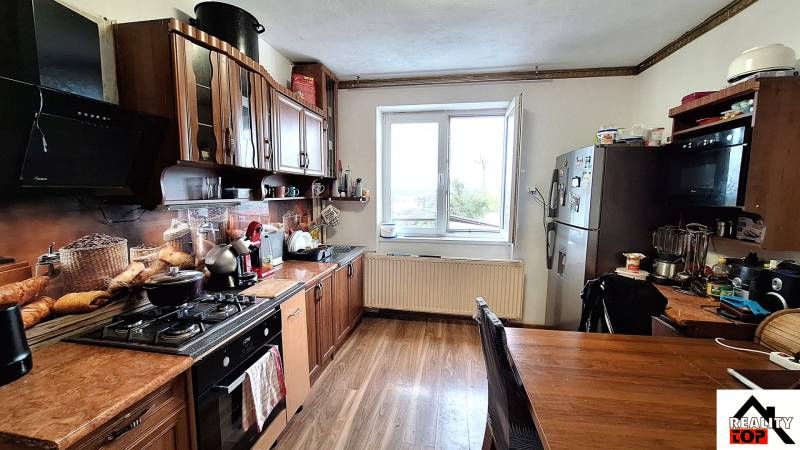 Kuchyně rodinného domu s kuchyňskou linkou, spotřebiči a podlahou s dřevěným dekorem.