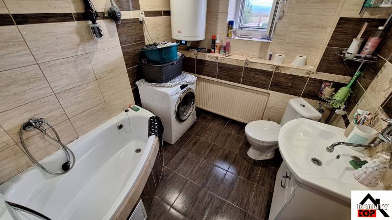 Koupelna v rodinném domě s vanou, pračkou a dekorativními hnědými obklady.