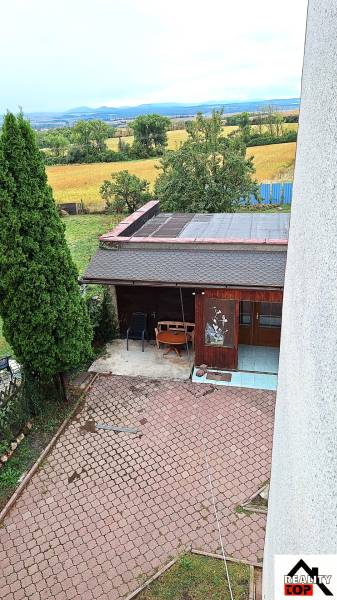 Zahrada rodinného domu v Zacharovcích s altánkem, stromy a výhledem na pole.