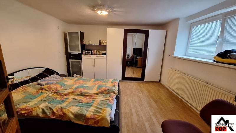 Ložnice s postelí, skříní a podlahou s dřevěným dekorem v rodinném domě.