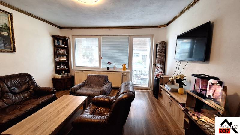 Obývací pokoj v rodinném domě s koženým nábytkem a podlahou s dřevěným dekorem.