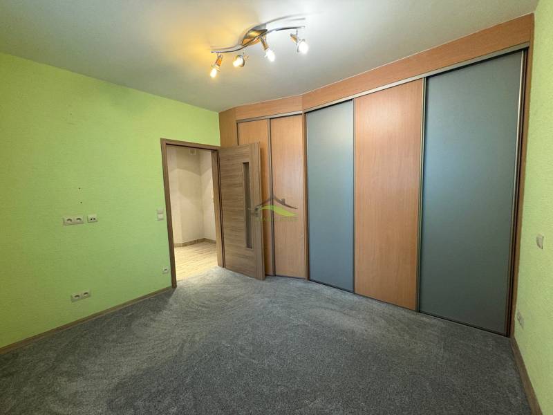 Pokoj v 3-pokojovém bytě s barevnou stěnou, skříní a světlým osvětlením.