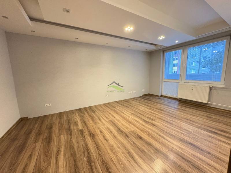 Obývací pokoj v 3-pokojovém bytě s podlahou s dřevěným dekorem a velkým oknem.