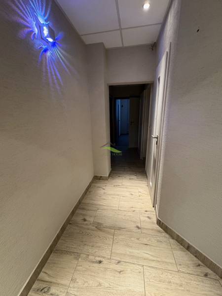 Chodba s podlahou s dřevěným dekorem, osvětlením a bílými stěnami ve 3-pokojovém bytě.