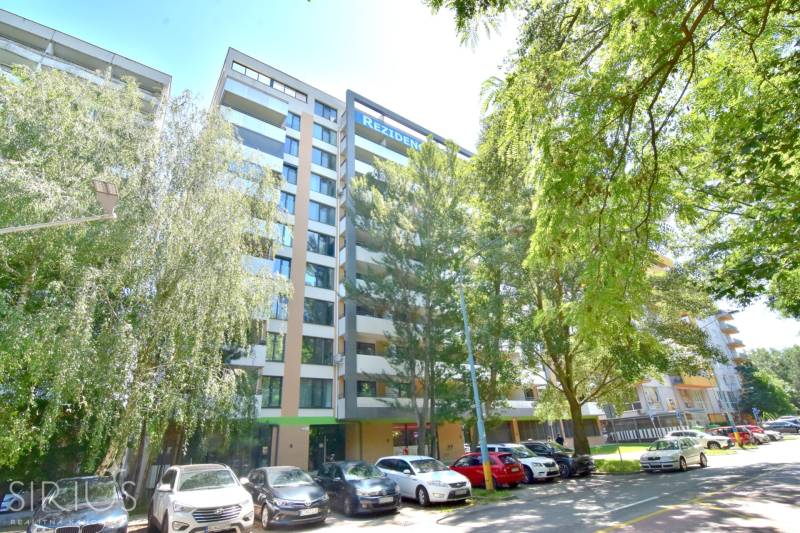 Bytový dům na Antolské ulici v Bratislavě - Petržalce, obklopený zelení a parkujícími auty.