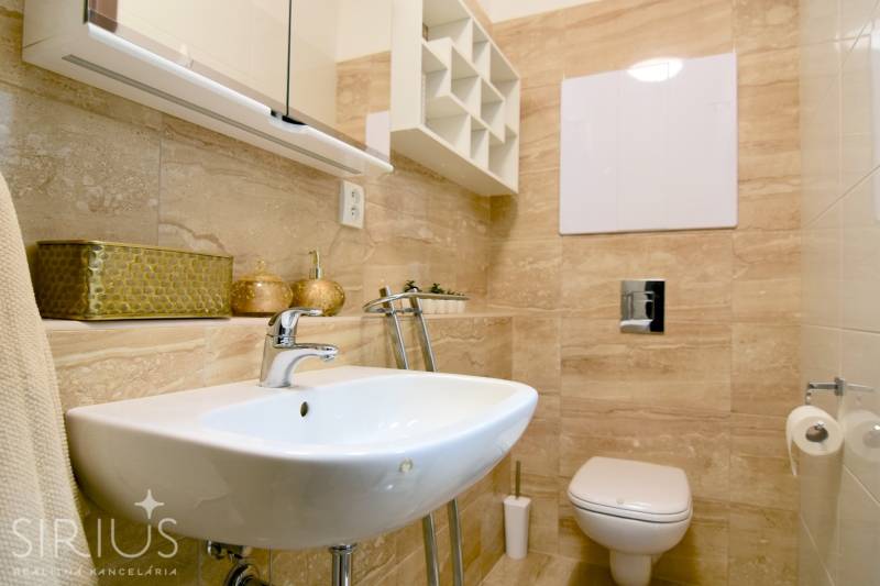 Koupelna v 2-pokojovém bytě s umyvadlem, toaletou a béžovým obkladem.