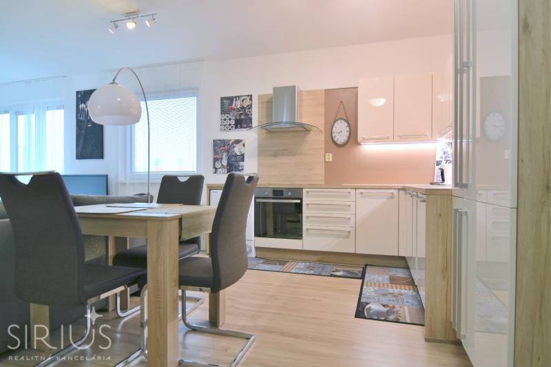 Moderní kuchyně s jídelním stolem, bílými skříňkami a podlahou s dřevěným dekorem v 2pokojovém bytě.