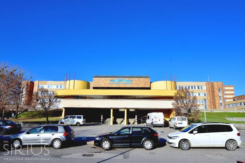 Budova nemocnice na Antolské ulici v Petržalce, Bratislava, s parkovištěm a auty.