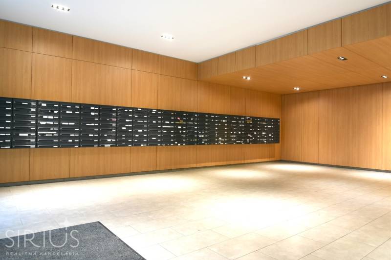 Obložené stěny dřevěným dekorem, poštovní schránky, dlažba, interiér 2-pokojového bytu.