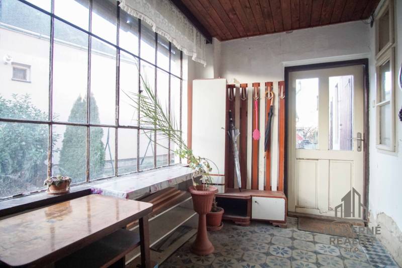 Interiér v rodinném domě s květináčem, stolem a věšákem na deštníky.