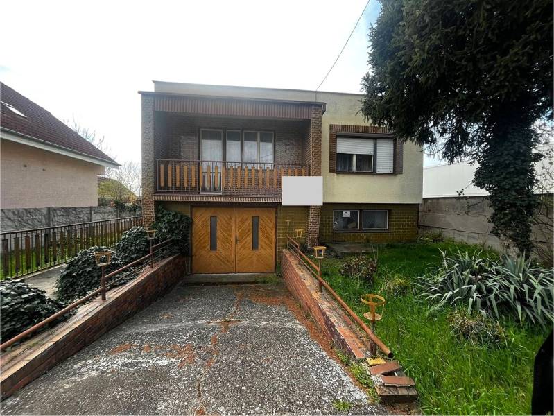 Rodinný dům v Šaľe s garáží, balkonem a zahradou, obklopený vegetací a plotem.