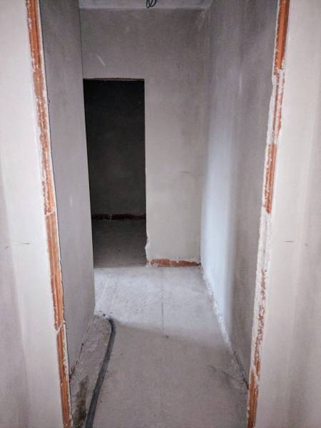 Úzká chodba v rozestavěném rodinném domě s odkrytou kabeláží na podlaze.