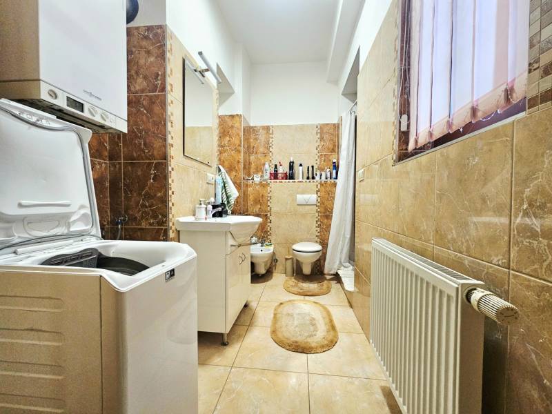 Koupelna s pračkou, umyvadlem, toaletou a světlou keramickou dlažbou ve 3-pokojovém bytě.