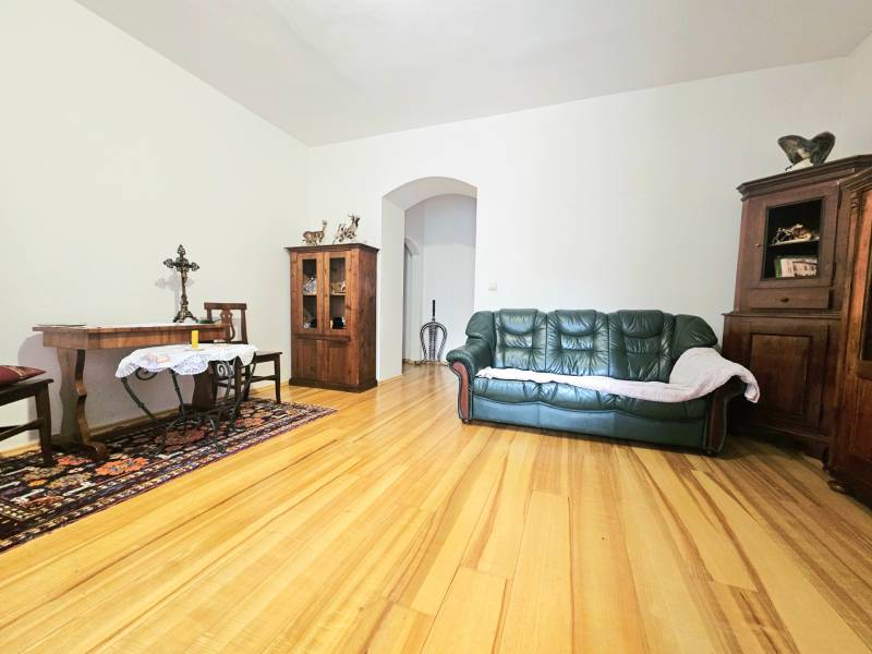 Obývací pokoj v 3-pokojovém bytě s podlahou s dřevěným dekorem, pohovkou a dřevěným nábytkem.