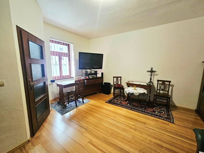 Pokoj v 3-pokojovém bytě s podlahou s dřevěným dekorem a televizí na stolku.