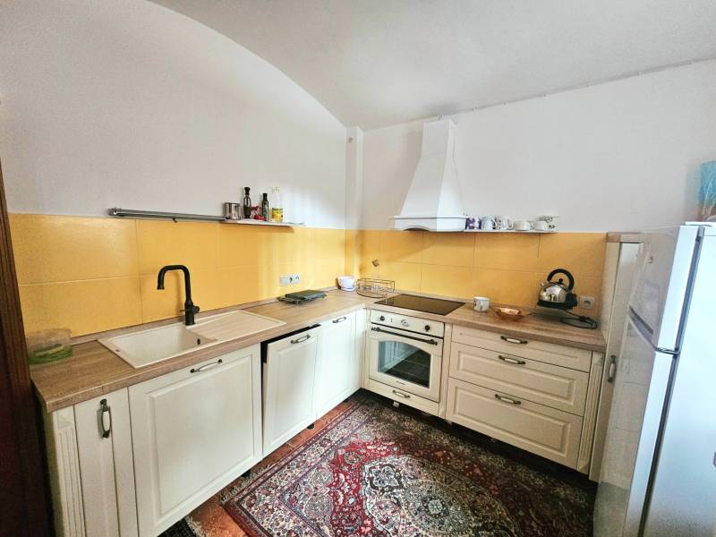 Kuchyně v 3-pokojovém bytě s krémovými skříňkami, žlutým obkladem a vzorovaným kobercem.